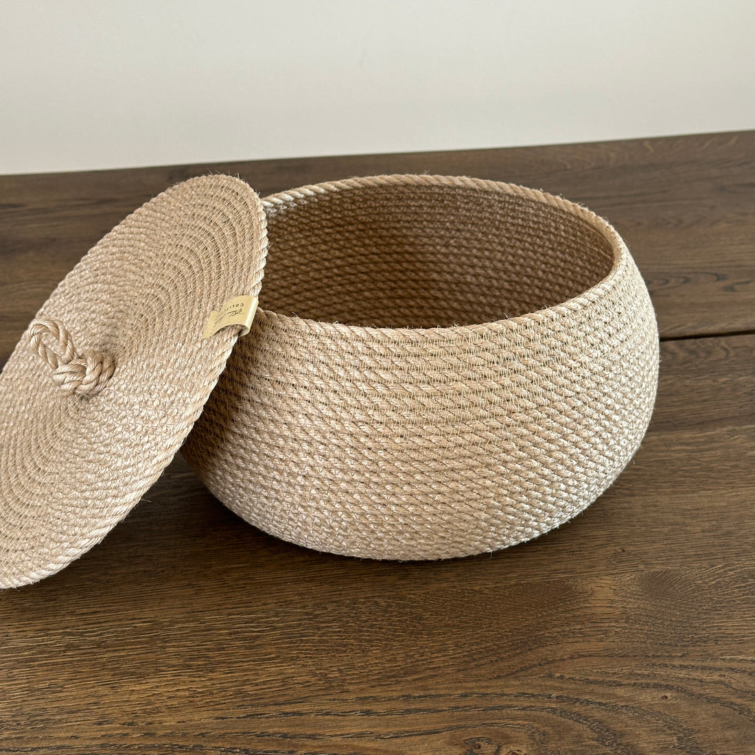 Lille tøndeformet kurv af jute med fladt låg og løkkehåndtag. Størrelse 22×14 cm. Et æstetisk og praktisk valg til opbevaring af småting og indretning.