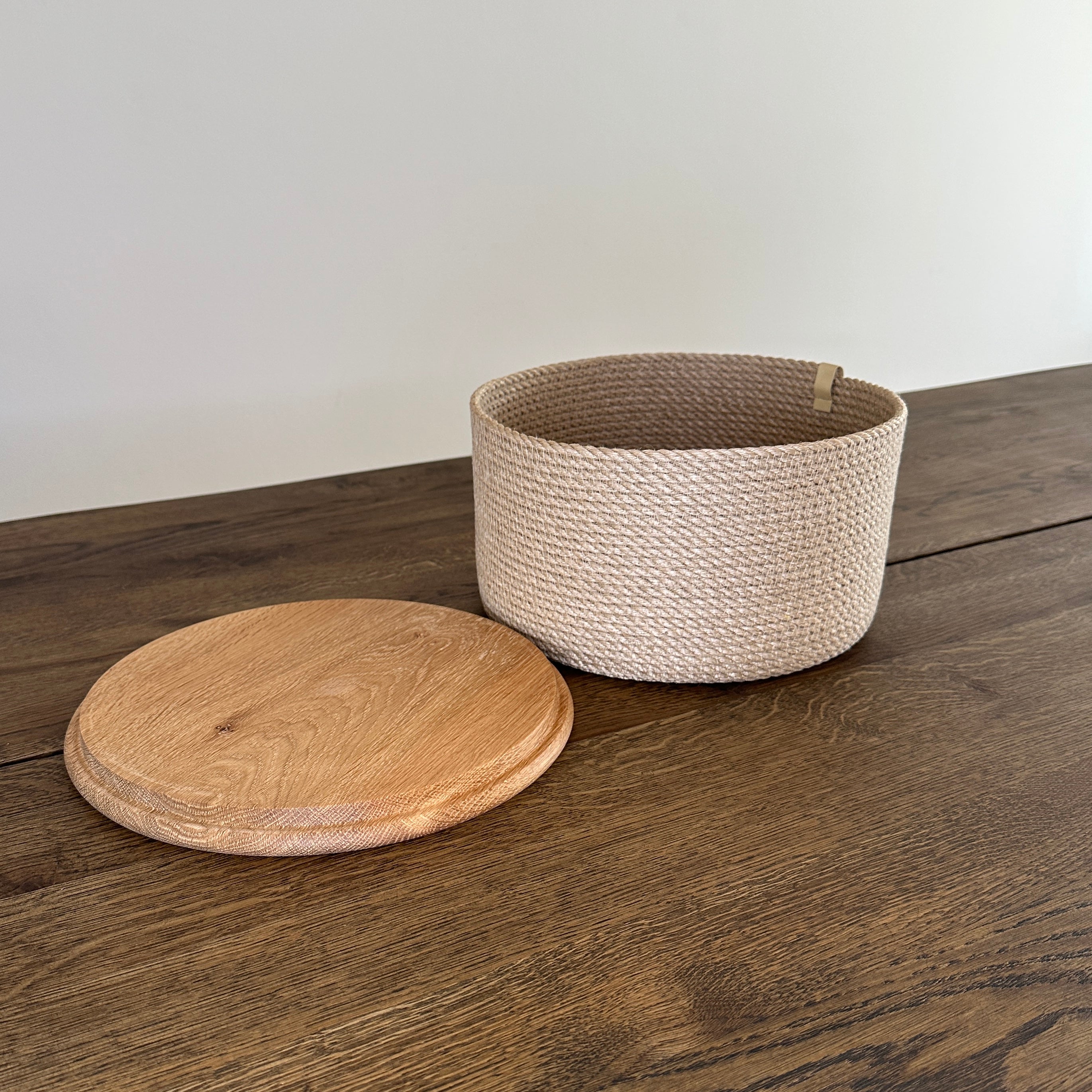 Elegant rund kurv af naturjute med låg i eg. Perfekt til servering af ost, brød eller frugt.