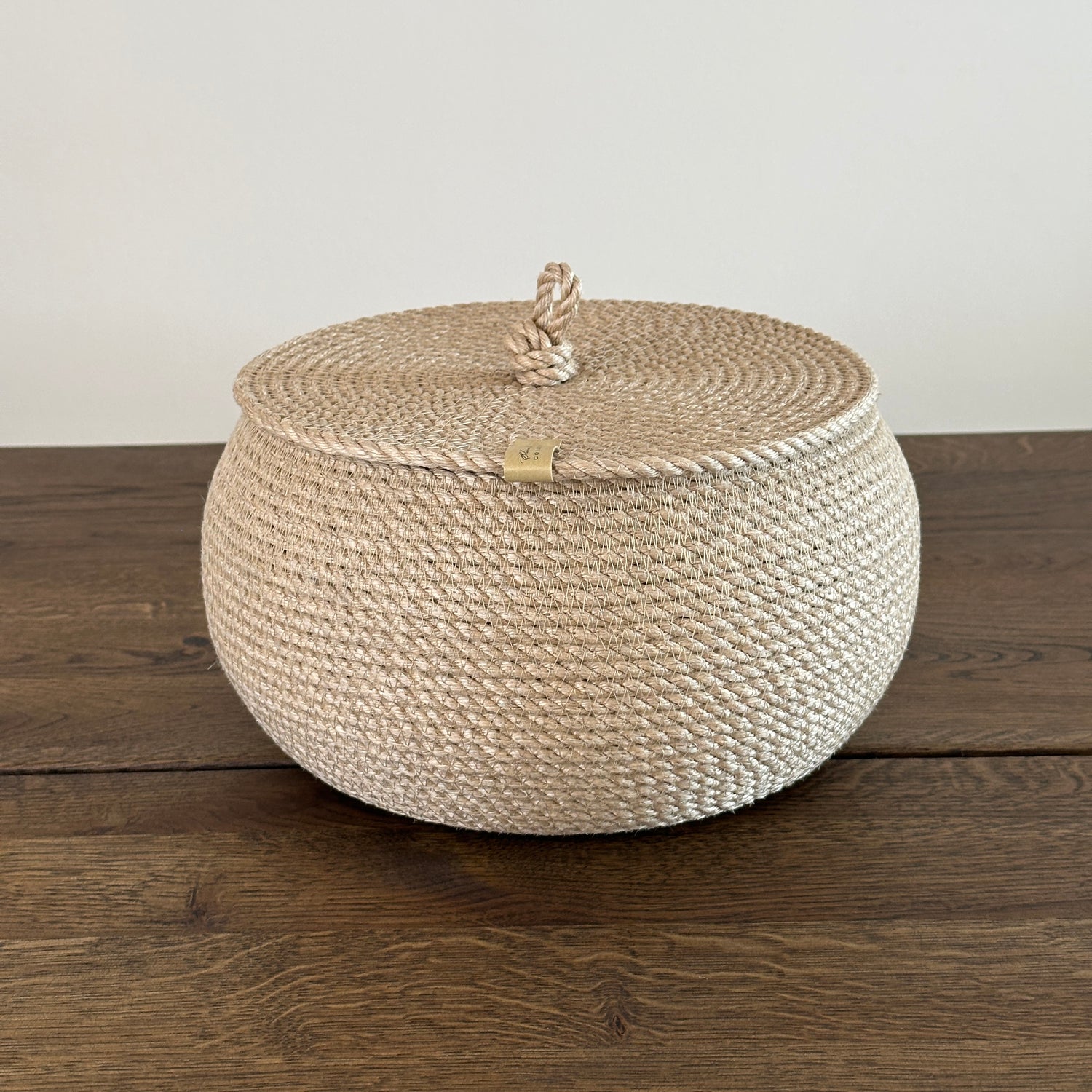 Kompakt jutekurv i tøndeform, diameter 22 cm, højde 14 cm. Fladt låg med løkkehåndtag giver både funktionalitet og stil. Håndlavet i gylden jute af premium kvalitet.