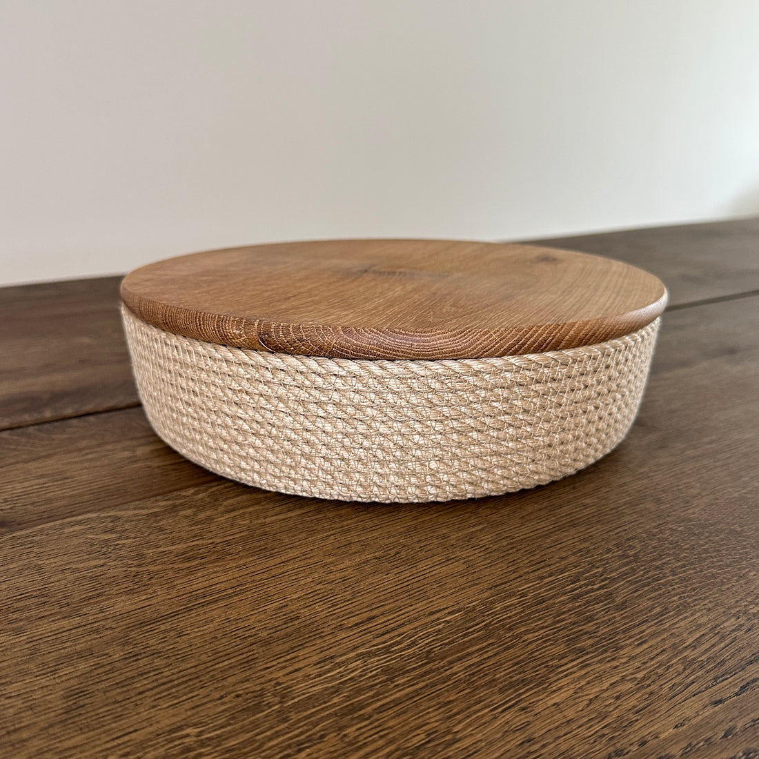 Lav rund kurv af naturjute med låg i egetræ. Perfekt til opbevaring og servering.