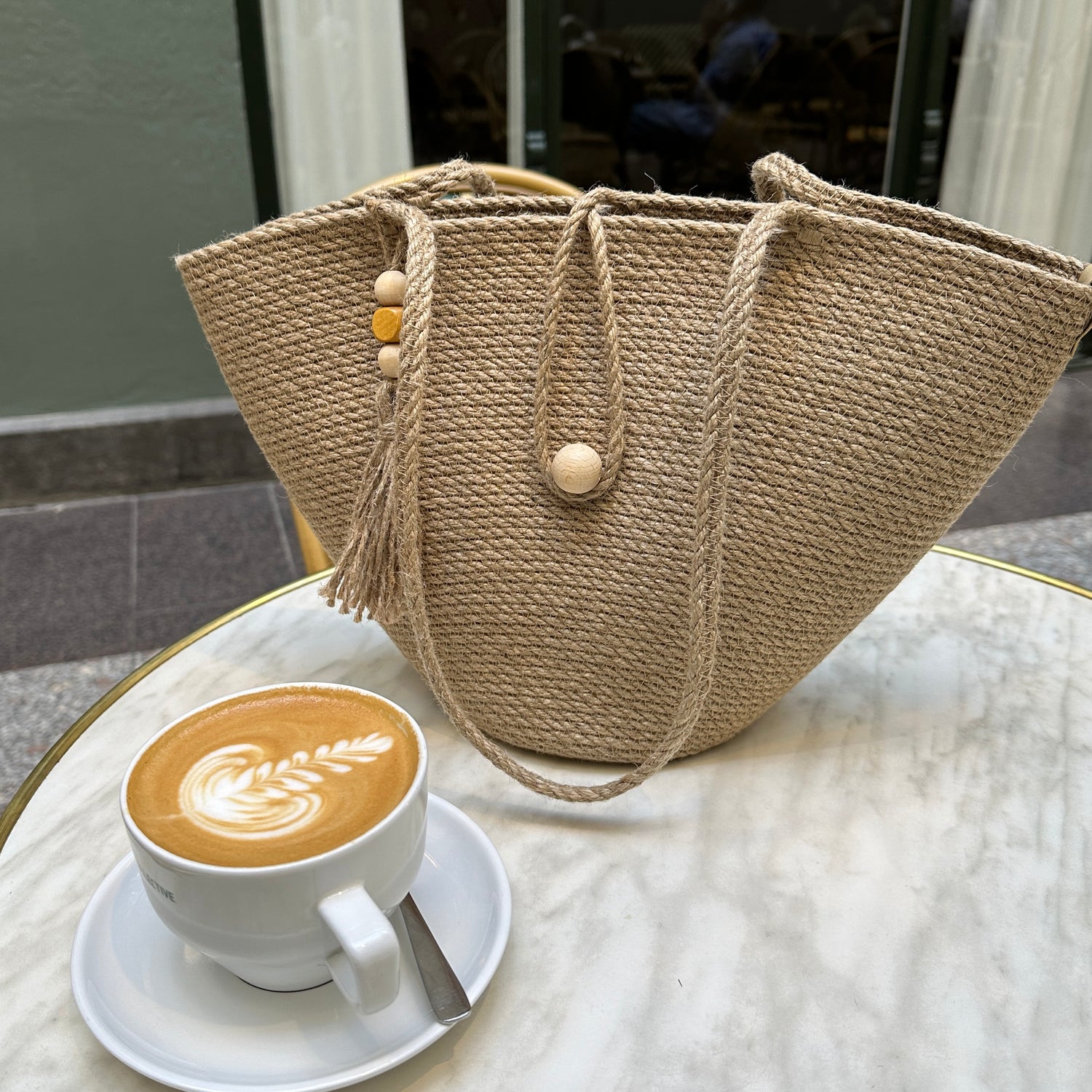 Taske i stærk jute med lange hanke, lukning med trækugle og dekorativ kvast med perler. En praktisk model til by og fritid.