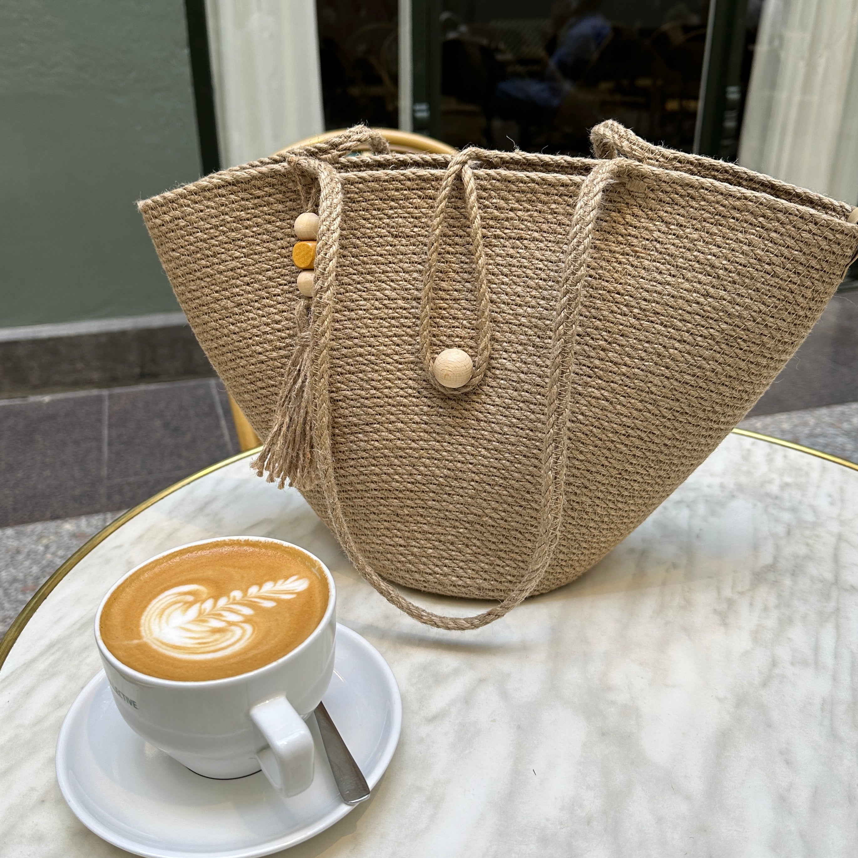 Taske i stærk jute med lange hanke, lukning med trækugle og dekorativ kvast med perler. En praktisk model til by og fritid.