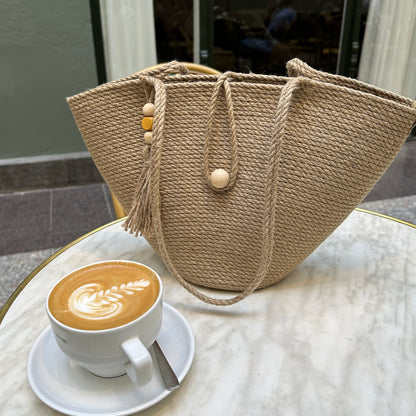 Taske i stærk jute med lange hanke, lukning med trækugle og dekorativ kvast med perler. En praktisk model til by og fritid.