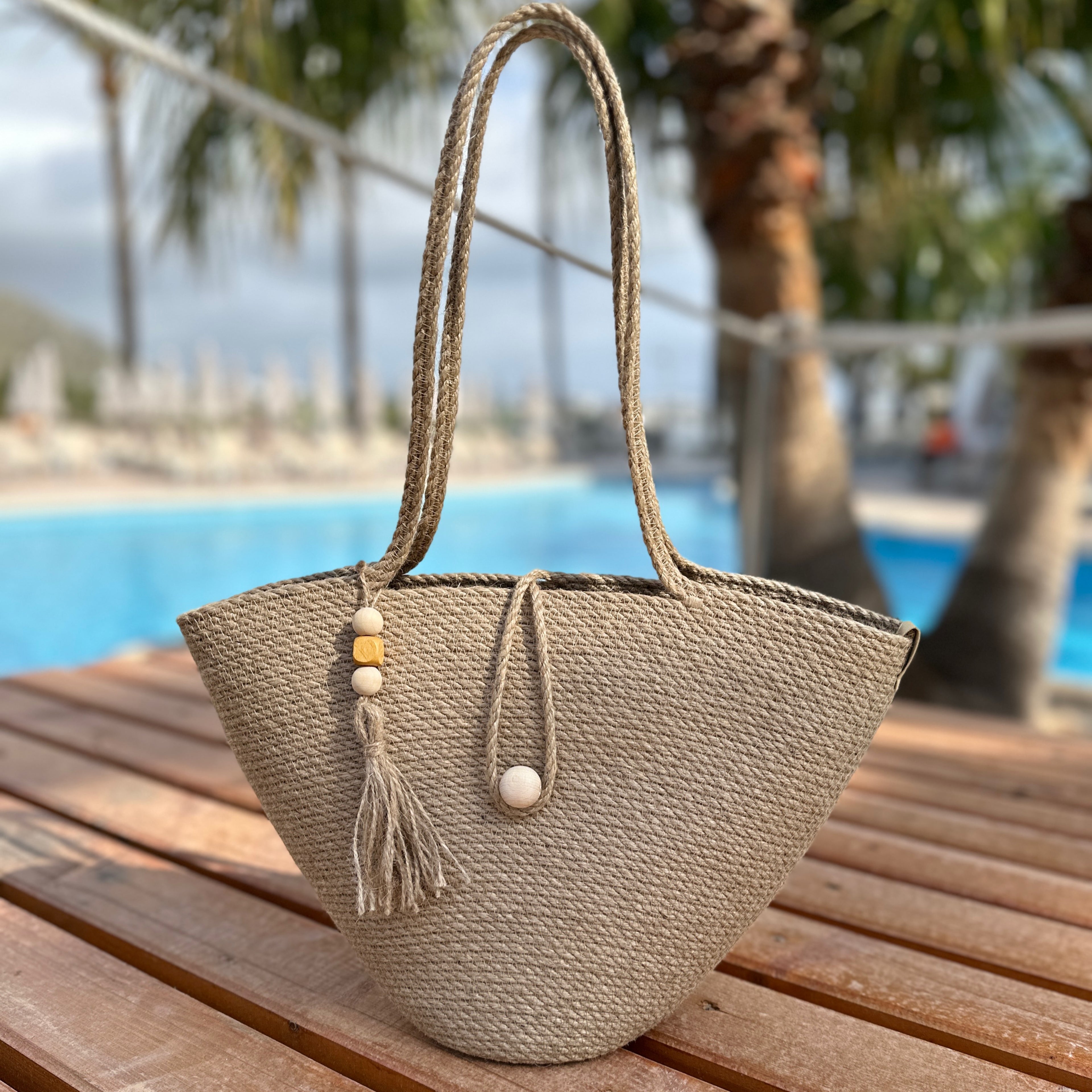 Rummelig håndlavet jute-taske med lange hanke, træknaplukning og dekorativ kvast med træelementer. Et naturligt og holdbart tilbehør.