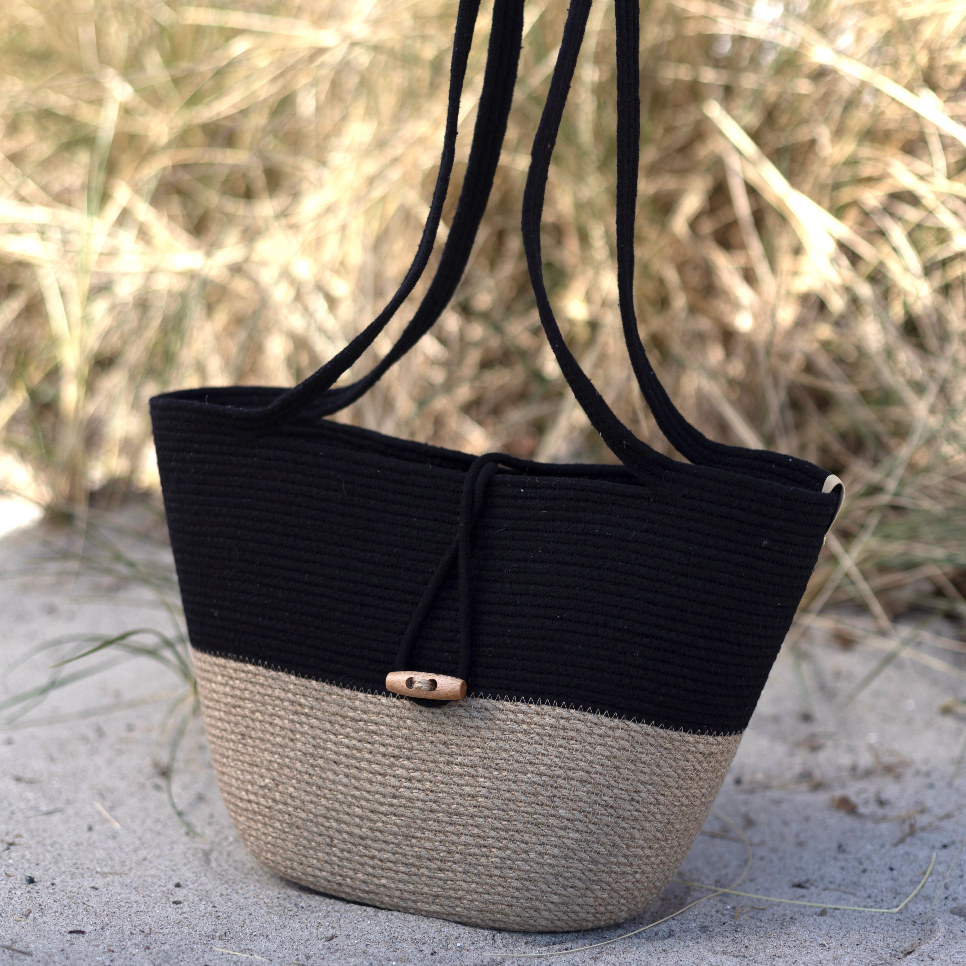 Håndlavet taske af jute og sort bomuldssnor med lange hanke og dekorativ lukning.
