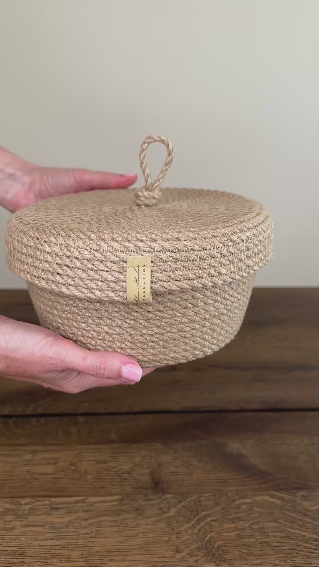 Videoen viser en kompakt rund jute kurv, 17×10 cm, med låg og praktisk holder i form af en løkke. Den præcise udførelse og de naturlige materialer gør produktet slidstærkt og langtidsholdbart.