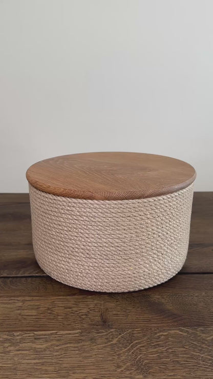 Cylinderformet jute kurv, 25 cm i diameter og 15 cm i højden, med låg af massivt egetræ. Det omhyggelige håndværk og premium jute fremhæver den høje kvalitet og holdbarhed.