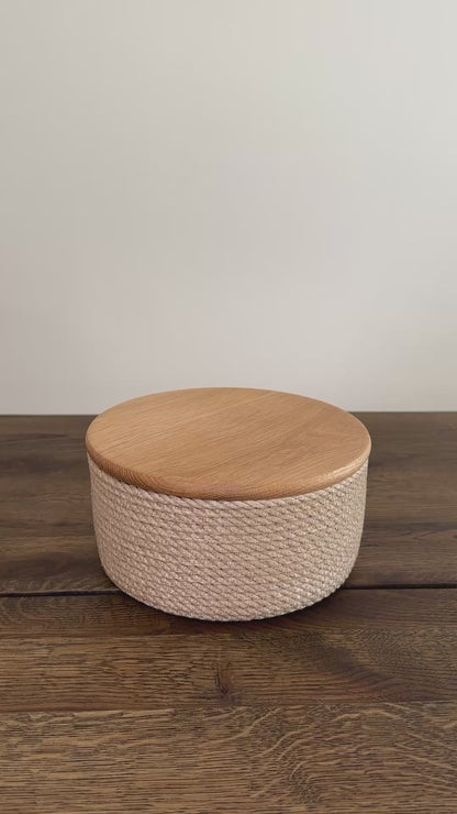 Videoen viser en jute kurv i mindre format, rund 20×10 cm, med låg af egetræ. Den præcise udførelse og de naturlige materialer gør produktet slidstærkt og langtidsholdbart.